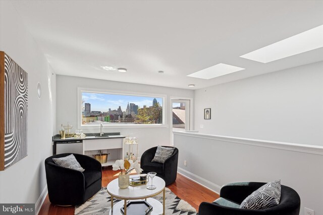 sitting room with a skylight, baseboards, wood finished floors, and a view of city
