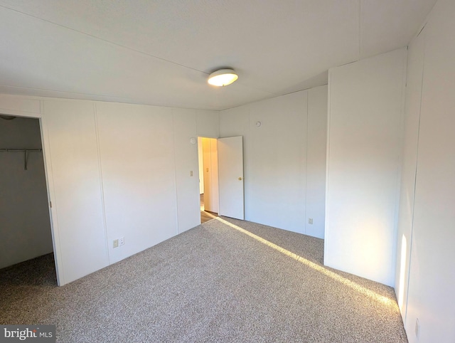 unfurnished bedroom with a spacious closet, a closet, and carpet