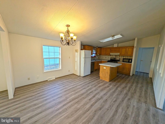 kitchen featuring a center island, light hardwood / wood-style flooring, backsplash, lofted ceiling with skylight, and black appliances