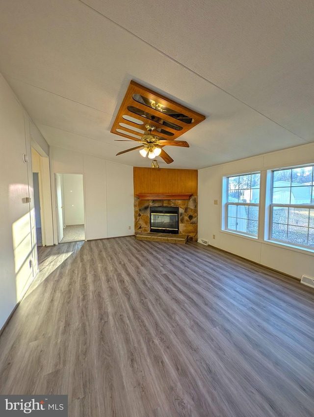 unfurnished living room with hardwood / wood-style floors, ceiling fan, and a stone fireplace