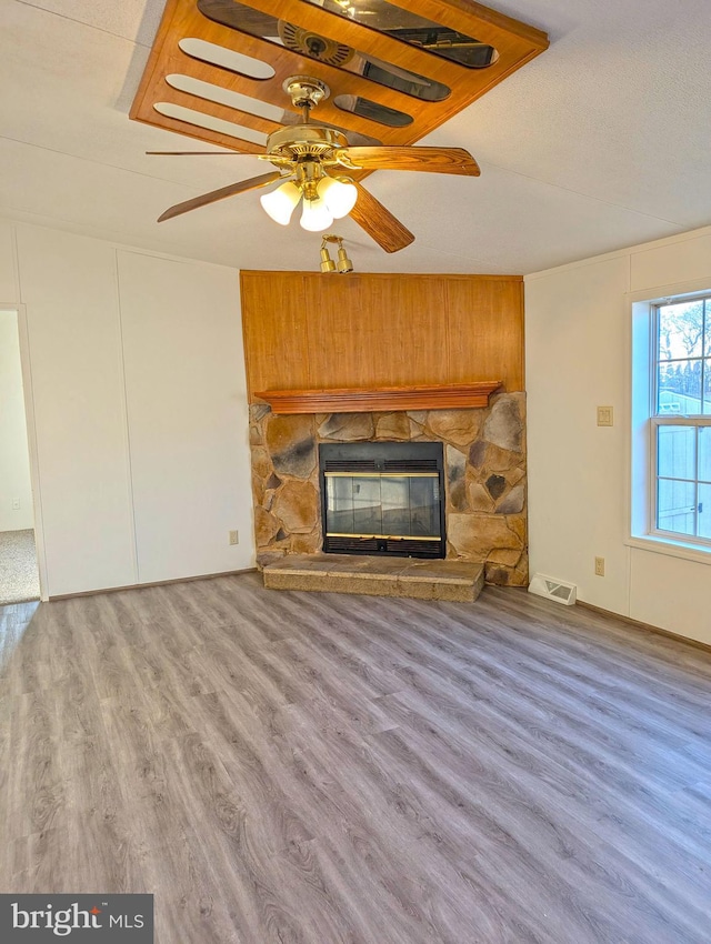 unfurnished living room featuring hardwood / wood-style floors, a stone fireplace, and ceiling fan