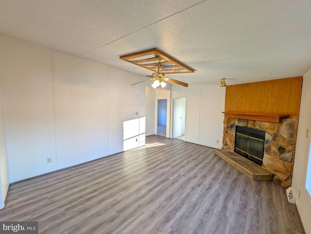 unfurnished living room featuring a stone fireplace, ceiling fan, light hardwood / wood-style floors, and a textured ceiling