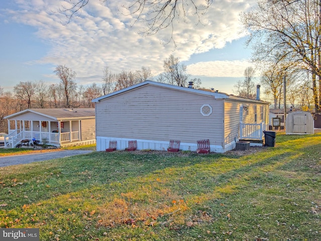 view of side of home with a lawn, covered porch, and a storage shed