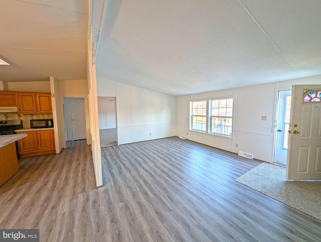 unfurnished living room with light hardwood / wood-style floors, lofted ceiling, and a textured ceiling