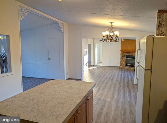 kitchen with a stone fireplace, light hardwood / wood-style flooring, white refrigerator, pendant lighting, and lofted ceiling