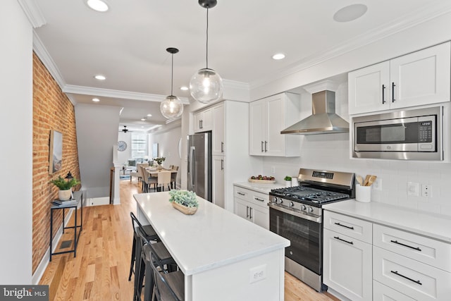 kitchen featuring white cabinets, wall chimney range hood, light hardwood / wood-style flooring, a kitchen island, and stainless steel appliances