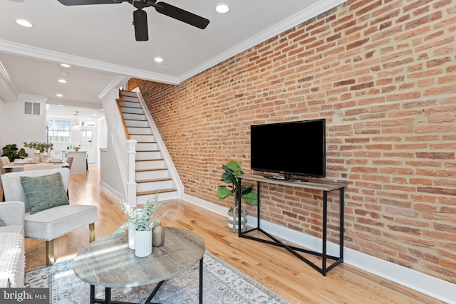 living room with light hardwood / wood-style flooring, ceiling fan, crown molding, and brick wall