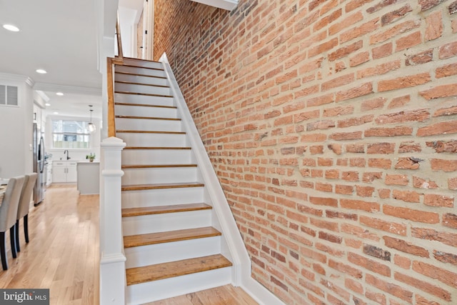 stairway featuring hardwood / wood-style flooring, sink, and brick wall