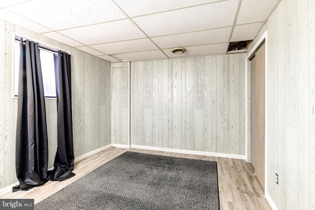 spare room with a paneled ceiling, wood walls, and light wood-type flooring