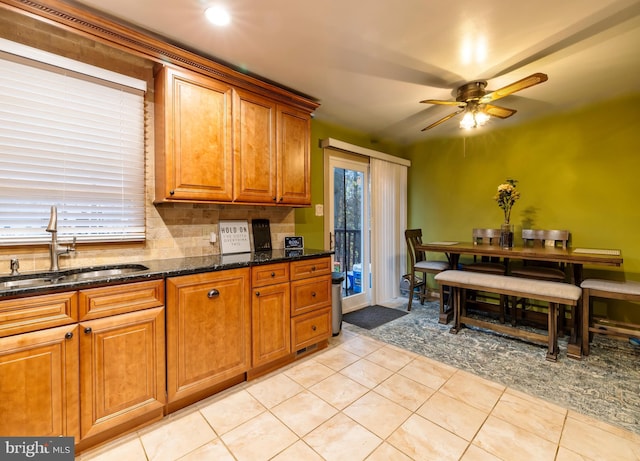 kitchen with light tile patterned floors, ceiling fan, dark stone counters, and sink