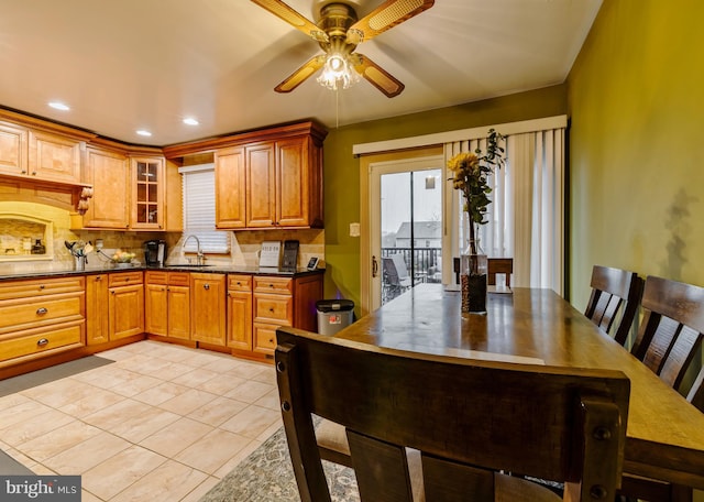 kitchen with sink, decorative backsplash, ceiling fan, dark stone countertops, and light tile patterned floors