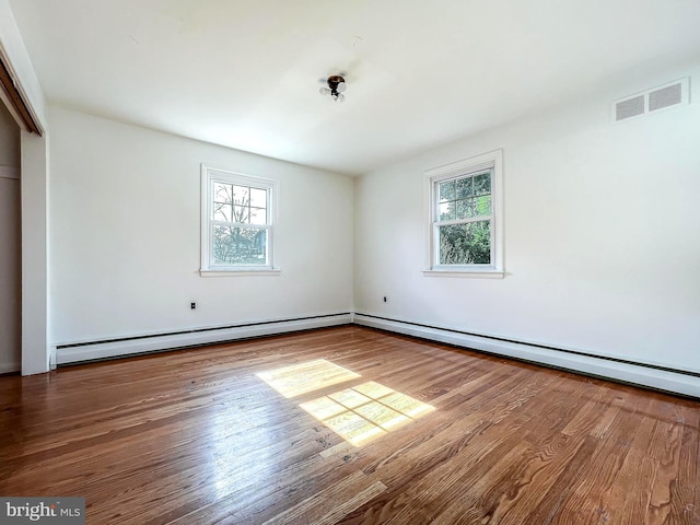 unfurnished bedroom with baseboard heating, multiple windows, and hardwood / wood-style flooring