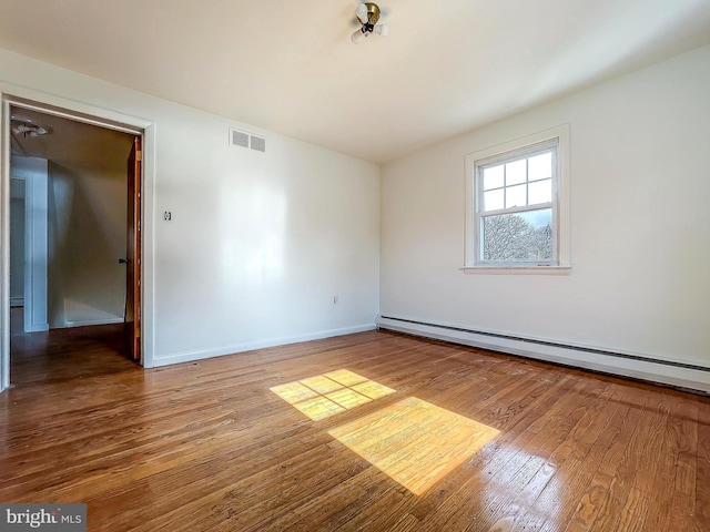 spare room featuring baseboard heating and wood-type flooring