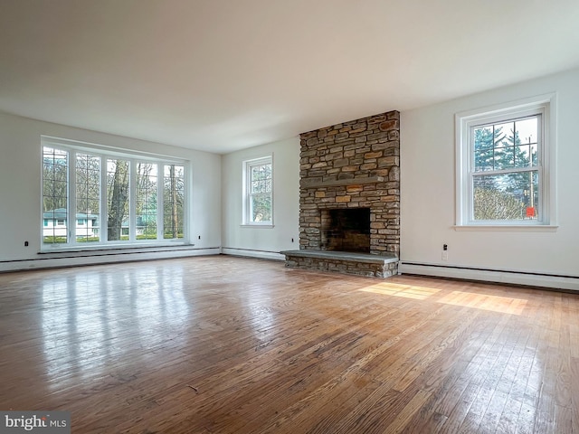 unfurnished living room with hardwood / wood-style flooring, a stone fireplace, baseboard heating, and a wealth of natural light