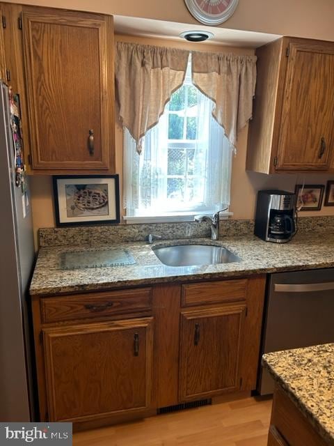 kitchen with stainless steel appliances, light stone countertops, sink, and light hardwood / wood-style floors