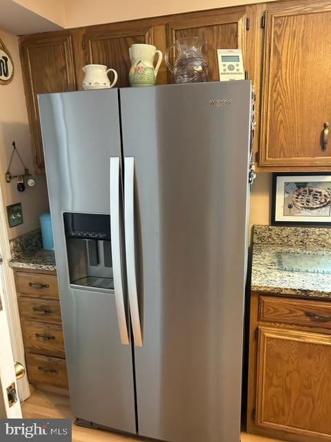 kitchen featuring stainless steel fridge with ice dispenser, light stone countertops, and light hardwood / wood-style floors