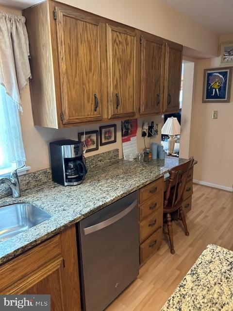 kitchen featuring dishwasher, light hardwood / wood-style floors, light stone countertops, and sink