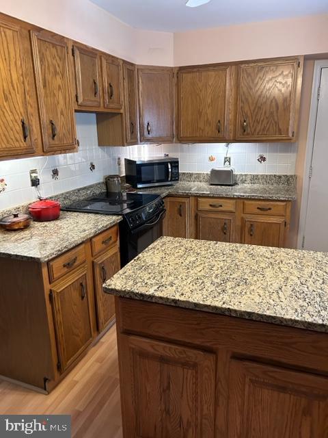 kitchen featuring black electric range, decorative backsplash, light wood-type flooring, and light stone countertops