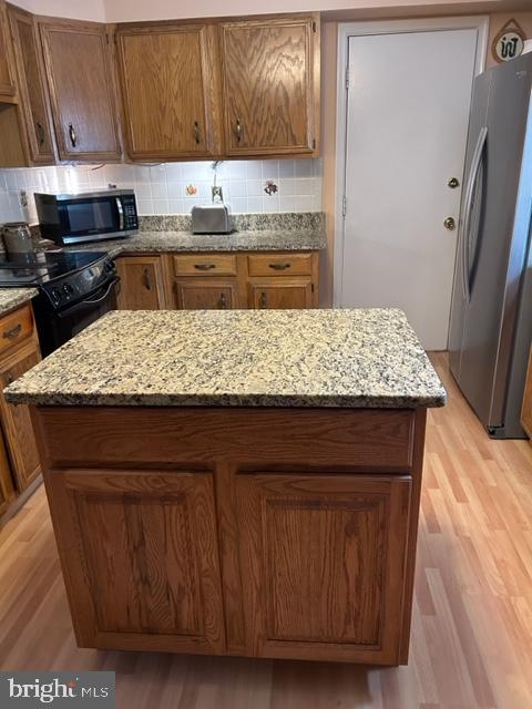 kitchen with light stone countertops, a kitchen island, light wood-type flooring, and appliances with stainless steel finishes