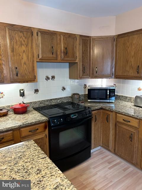 kitchen featuring light stone countertops, black range with electric cooktop, light hardwood / wood-style floors, and tasteful backsplash