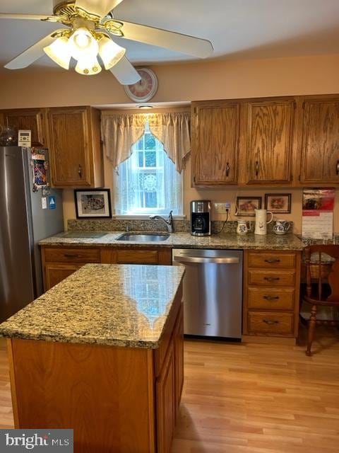 kitchen with dishwasher, light stone countertops, light wood-type flooring, and sink