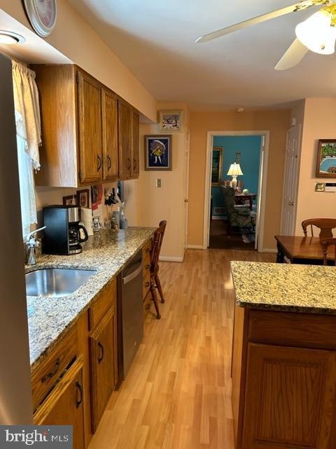 kitchen with dishwasher, sink, ceiling fan, light hardwood / wood-style floors, and light stone counters