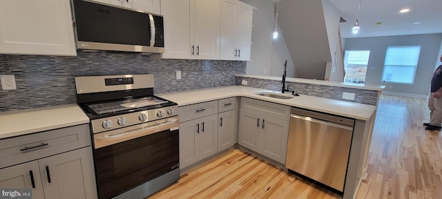 kitchen with pendant lighting, appliances with stainless steel finishes, sink, light wood-type flooring, and tasteful backsplash