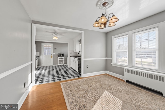 interior space with wood-type flooring, ceiling fan with notable chandelier, radiator, and sink