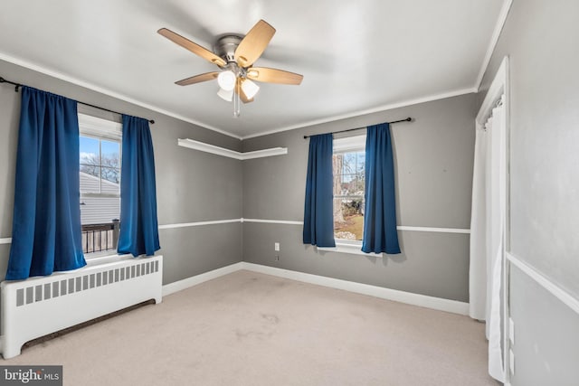 spare room featuring radiator heating unit, light colored carpet, a healthy amount of sunlight, and ornamental molding