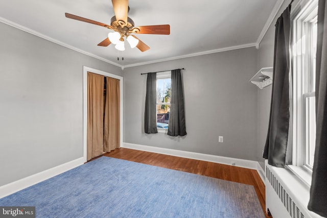 unfurnished bedroom featuring ceiling fan, crown molding, hardwood / wood-style flooring, radiator heating unit, and a closet