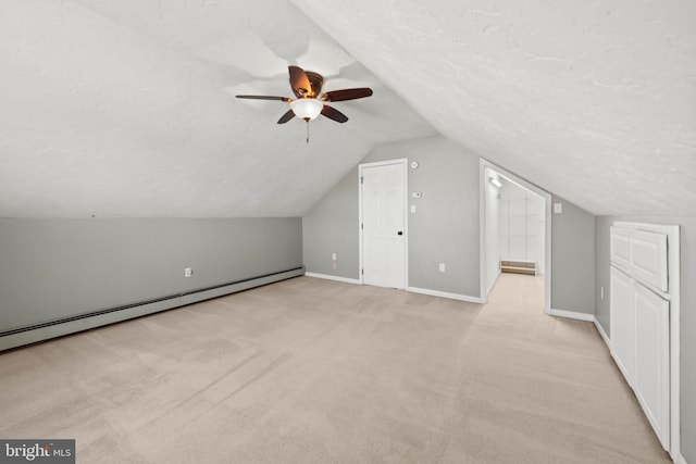 bonus room featuring ceiling fan, a baseboard heating unit, light colored carpet, a textured ceiling, and vaulted ceiling