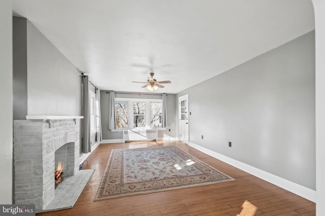 unfurnished living room with ceiling fan, wood-type flooring, a fireplace, and radiator