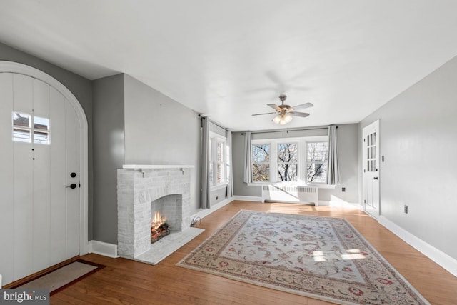 unfurnished living room featuring ceiling fan, light hardwood / wood-style floors, radiator heating unit, and a brick fireplace