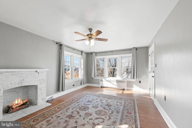 living room with radiator, a wealth of natural light, hardwood / wood-style floors, and a brick fireplace