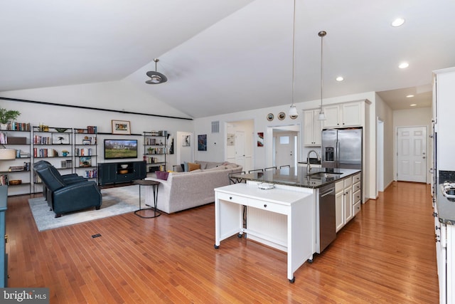 kitchen featuring a kitchen island with sink, dark stone counters, white cabinets, vaulted ceiling, and light hardwood / wood-style floors