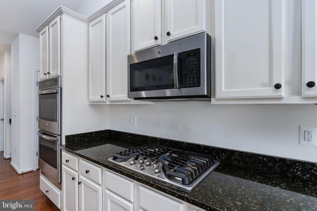 kitchen with appliances with stainless steel finishes, dark hardwood / wood-style floors, white cabinetry, and dark stone counters