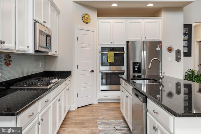 kitchen with white cabinetry, stainless steel appliances, dark stone countertops, light hardwood / wood-style floors, and decorative backsplash