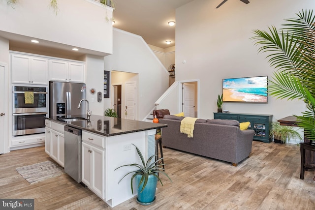 kitchen with appliances with stainless steel finishes, light wood-type flooring, a high ceiling, white cabinetry, and an island with sink