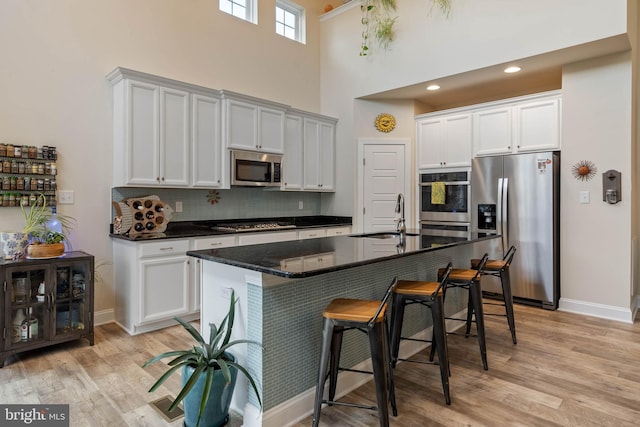 kitchen with appliances with stainless steel finishes, light wood-type flooring, a high ceiling, and sink