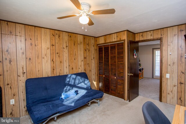 sitting room featuring wooden walls, carpet flooring, and a ceiling fan