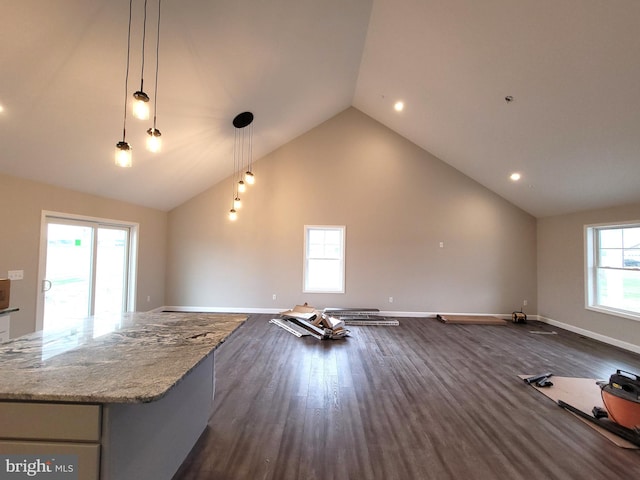 interior space with high vaulted ceiling, hanging light fixtures, a center island, light stone countertops, and dark wood-type flooring