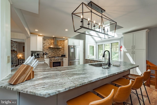 kitchen with appliances with stainless steel finishes, sink, white cabinetry, and wall chimney range hood