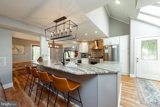 kitchen featuring white cabinets, sink, wall chimney exhaust hood, appliances with stainless steel finishes, and decorative light fixtures