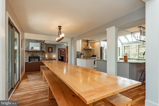 dining room with light hardwood / wood-style floors, a stone fireplace, and a notable chandelier