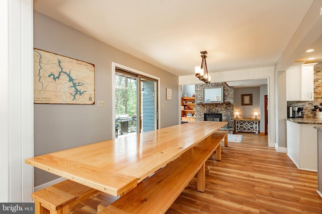 dining space with a notable chandelier, a stone fireplace, and light hardwood / wood-style flooring