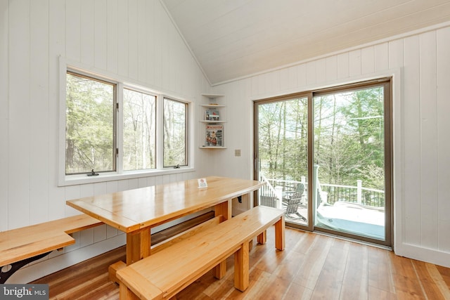 dining room featuring wooden walls, vaulted ceiling, a wealth of natural light, and light hardwood / wood-style flooring