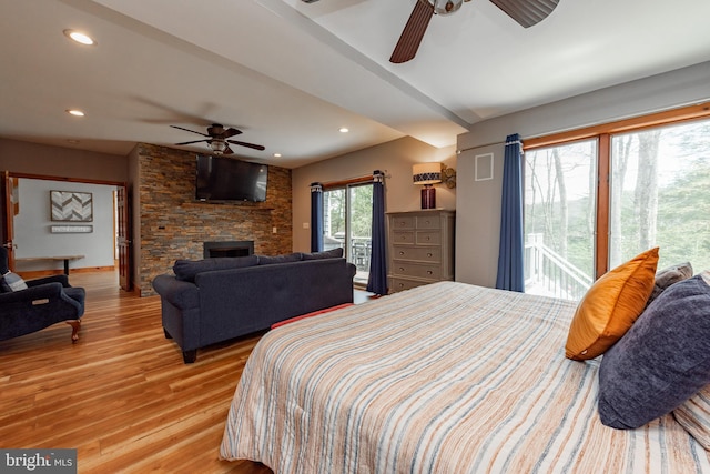 bedroom featuring access to exterior, ceiling fan, light hardwood / wood-style flooring, and a stone fireplace