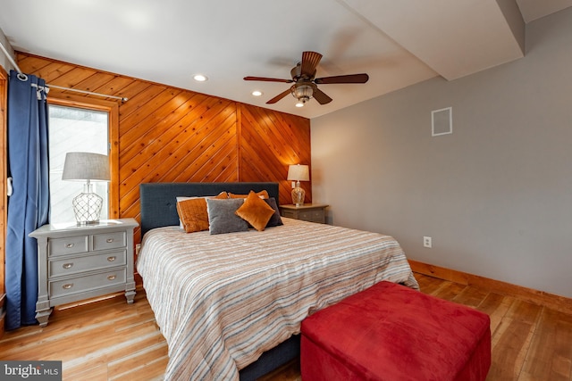 bedroom with ceiling fan, wooden walls, and light hardwood / wood-style flooring