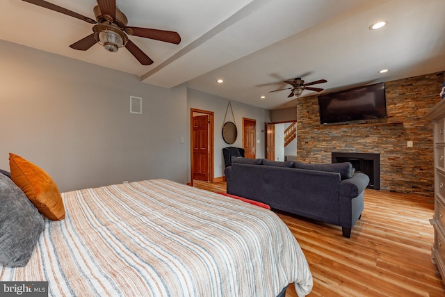 bedroom with ceiling fan, a stone fireplace, and light hardwood / wood-style flooring