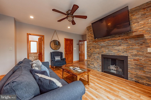 living room with a stone fireplace, ceiling fan, and hardwood / wood-style flooring